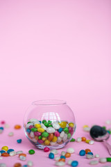 colorful candy in clear wrappers piled in a glass vase isolated on pink background
