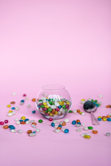 colorful candy in clear wrappers piled in a glass vase isolated on pink background