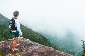 Caucasian female backpacker standing on a rock looking over a valley covered in clouds on Bokor Mountain in Cambodia