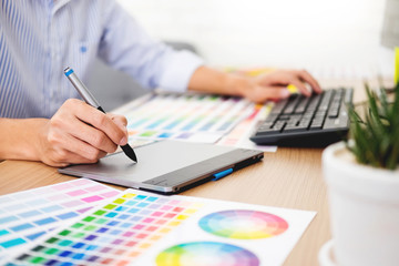 designer Editor at work drawing sketches a new project on graphic tablet and color palette sitting at desk with computer at studio or office