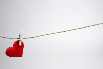 Single lonely red heart hanging from string by clothes peg on white background. Romantic...