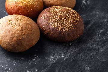 Yellow and brown sesame buns on a black background. Flour and bakery products. Fresh bread. Copy space
