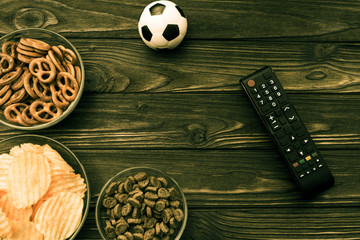 snacks, chips, crackers, soccer ball, TV remote on a wooden table background. football match, fans