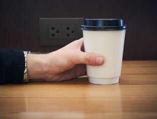 Hand hold paper coffee cup for take away on the wooden table