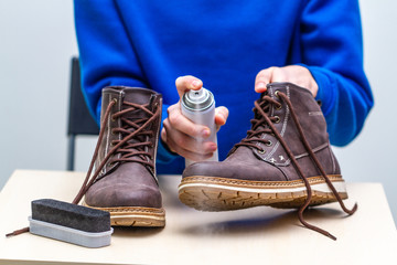 A person is cleaning and spraying agent on men's suede casual boots for protection from moisture and dirt. Shoe care 