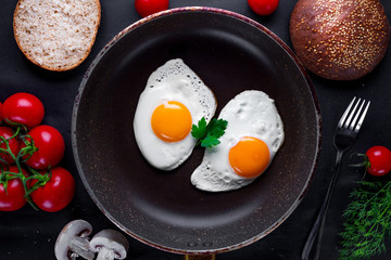 Homemade, fresh, fried eggs in a frying pan with dill, parsley, tomatoes and sesame bun for a healthy breakfast. Top view. Protein food