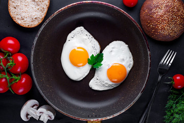 Homemade, fresh, fried eggs in a frying pan with dill, parsley, tomatoes and sesame bun for a healthy breakfast. Top view. Protein food