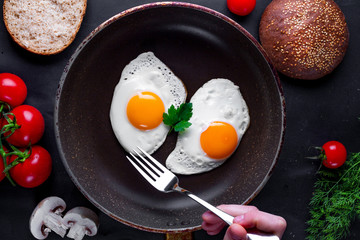 Fried eggs in a frying pan with dill, parsley, tomatoes cherry and sesame buns for a healthy breakfast. Top view. Protein food