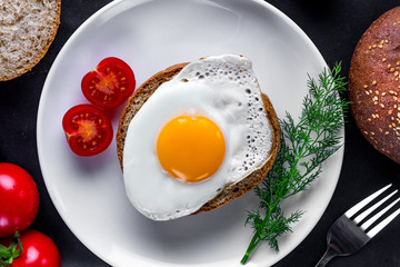 Homemade, fried chicken egg on a plate with dill, tomatoes cherry and sesame bun for a healthy breakfast. Protein food. Eggs sandwiches. Top view