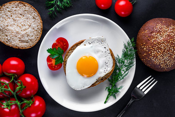 Homemade, fried chicken egg on a plate with dill, parsley, tomatoes cherry and sesame bun for a healthy breakfast. Protein food. Eggs sandwiches. Top view