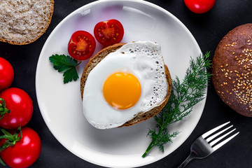 Homemade, fried chicken egg on a plate with dill, parsley, tomatoes cherry and sesame bun for a healthy breakfast. Protein food. Eggs sandwiches. Top view