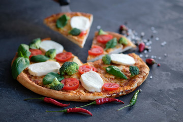 Sliced pizza with Mozzarella cheese, tomatoes, broccoli, Spices and fresh basil. Italian pizza. Pizza on black stone background