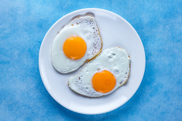 Fried chicken eggs on a plate for a healthy breakfast on a blue background. Protein food. Top view