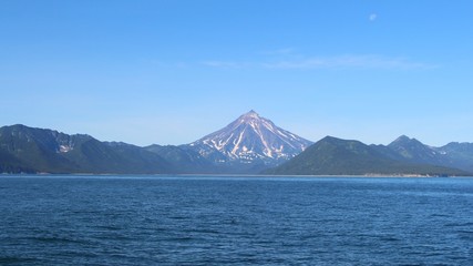 Fototapeta premium View of Vilyuchinsky volcano (also called Vilyuchik) from water. It's a stratovolcano in the southern part of Kamchatka Peninsula, Russia. Moon is visible in the sky.