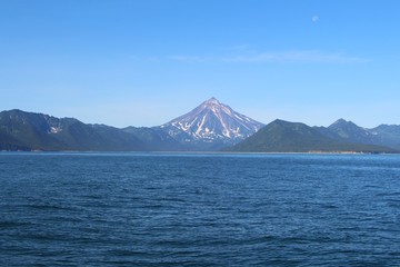 View of Vilyuchinsky volcano (also called Vilyuchik) from water. It's a stratovolcano in the southern part of Kamchatka Peninsula, Russia. Moon is visible in the sky.