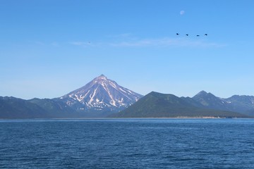 View of Vilyuchinsky volcano (also called Vilyuchik) from water. It's a stratovolcano in the southern part of Kamchatka Peninsula, Russia. Moon is visible in the sky.