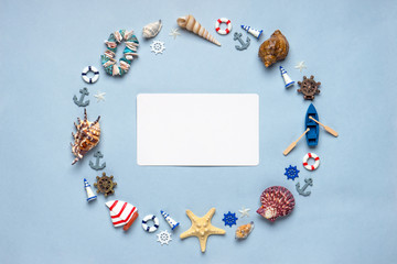 Fototapeta premium Round frame made of decorative items and miniature toys: seashells, seastars, vessel, boat, anchors, steering wheels, life buoys. Empty white paper card, mock-up. Summer vacation, sea travel concept