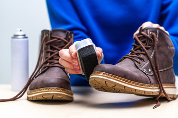 A person is cleaning men's suede casual boots with brush and spray. Shoe care. Footwear moisture and dirt protection