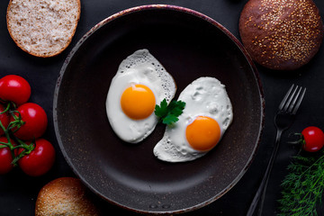 Homemade, fresh, fried eggs in a frying pan with dill, parsley, tomatoes and sesame bun for a healthy breakfast. Top view. Protein food
