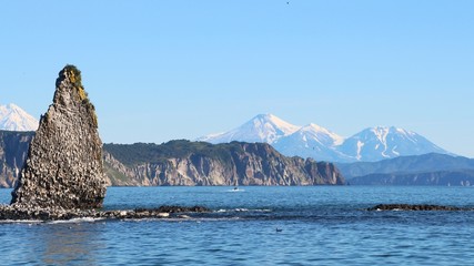 Rocky reef by Starichkov island near Kamchatka Peninsula, Russia. Avachinsky and Kozelsky volcanoes are visible in the background.