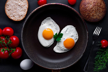 Homemade, fresh, fried eggs in a frying pan with dill, parsley, tomatoes and sesame bun for a healthy breakfast. Top view. Protein food