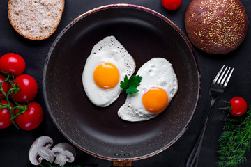 Fried eggs in a frying pan with dill, parsley, tomatoes cherry and sesame bun for a healthy breakfast. Top view. Protein food