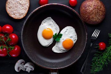 Homemade, fresh, fried eggs in a frying pan with dill, parsley, tomatoes and sesame bun for a healthy breakfast. Top view. Protein food