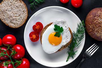 Homemade, fried chicken egg on a plate with dill, parsley, tomatoes cherry and sesame bun for a healthy breakfast. Protein food. Eggs sandwiches. Top view