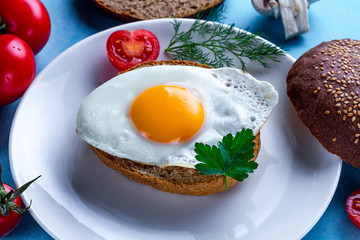 Homemade, fried chicken egg on a plate with dill, parsley, tomatoes cherry and sesame bun for a healthy breakfast. Protein food. Eggs sandwiches.