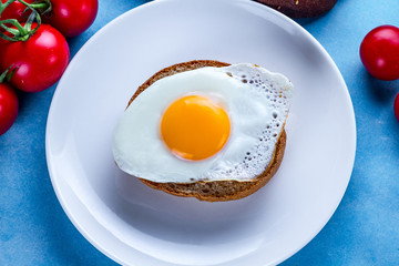 Homemade, fried egg on a plate with tomatoes and bun for a healthy breakfast. Protein food. Eggs sandwiches. Top view