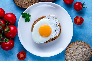 Homemade, fresh, fried chicken eggs on a plate with parsley, tomatoes cherry and sesame bun for a healthy breakfast. Protein food. Eggs sandwiches.