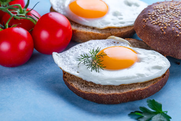 Buns with homemade, fried chicken eggs for a healthy breakfast on a blue background. Protein food. Eggs sandwiches