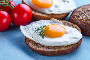 Buns with homemade, fried chicken eggs for a healthy breakfast on a blue background. Protein food. Eggs sandwiches