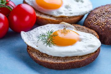 Buns with homemade, fried chicken eggs sprinkled with spices and salt for a breakfast on a blue background. Protein food. Eggs sandwiches