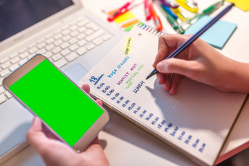 Woman hand writing in agenda consulting a mobile phone on a desk at home or office