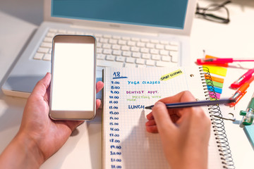 Woman hand writing in agenda consulting a mobile phone on a desk at home or office