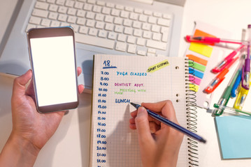 Woman hand writing in agenda consulting a mobile phone on a desk at home or office