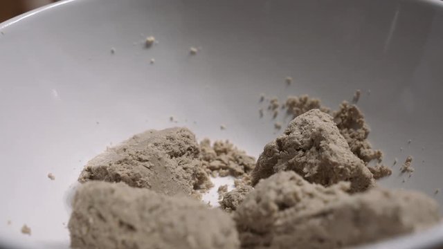 A man with a spoon breaks halva into small pieces in a white deep plate