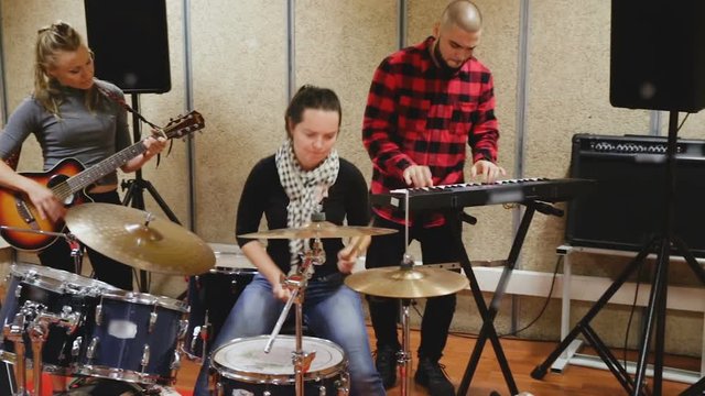 Rehearsal of music group. Rock band with emotional female drummer playing in recording studio