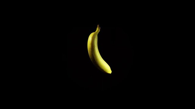 An isolated ripe yellow banana rotates clockwise against a black background, seamless looping.