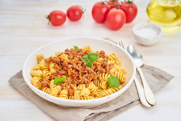 Bolognese pasta. Fusilli with tomato sauce, ground minced beef. Traditional italian cuisine. White wooden table. Side view.