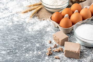 Baking ingredients of pressed yeast, eggs, sugar, milk and flour for Easter baking on gray background.