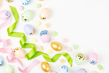 Festive Happy Easter background with decorated eggs, flowers, candy and ribbons in pastel colors on white. Copy space