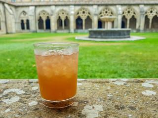 glass with brown drink supported on stone with monastery cloister background.