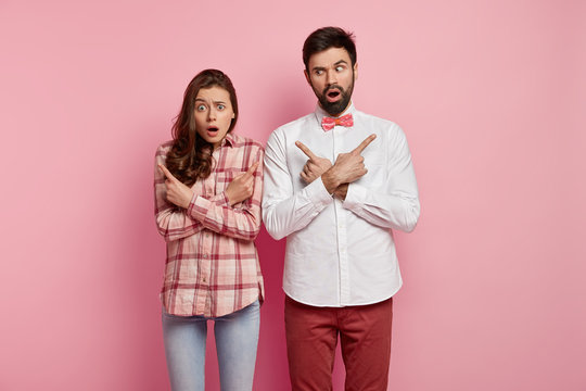 Isolated Shot Of Indecisive Family Couple Cross Hands Over Chest, Puzzled Between Two Choices, Cant Decide What Is Better, Have Surprised Frightened Expressions, Model Against Pink Background