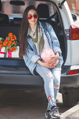 Young attractive woman in the car with presents box, gift and flowers. Beautiful lady in spring time with bouquet of tulips. Female in the automobile. © olenachukhil