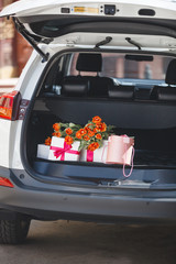 present boxes in the car. Gifts in automobile trunk. Tulip bouquet in the luggage boot.