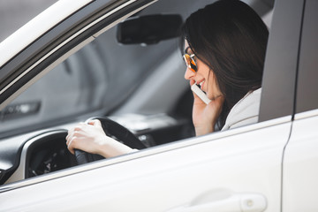 Attractive young woman talking on the mobile phone near the car. Confident lady having a cell phone...