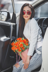 Young attractive woman in the car with presents box, gift and flowers. Beautiful lady in spring time with bouquet of tulips. Female in the automobile. © olenachukhil
