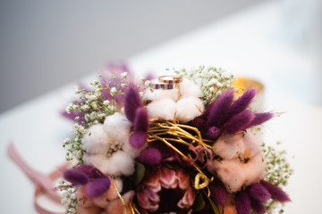  wedding rings next to purple  bouquet laying on the table